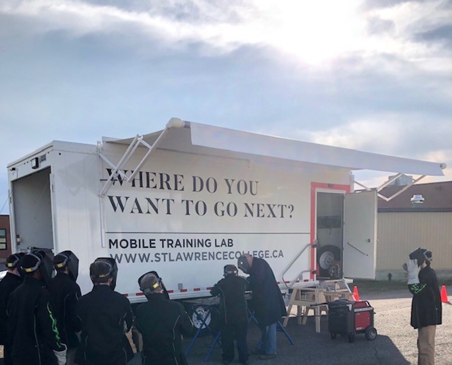 students in welding protective equipment stand in the sunshine outside of the mobile skills lab